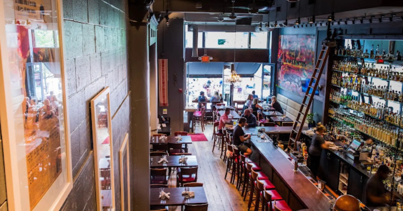 An inviting, dimly lit bar with a warm atmosphere, featuring a massive spirits collection and people enjoying drinks at the bar and tables.