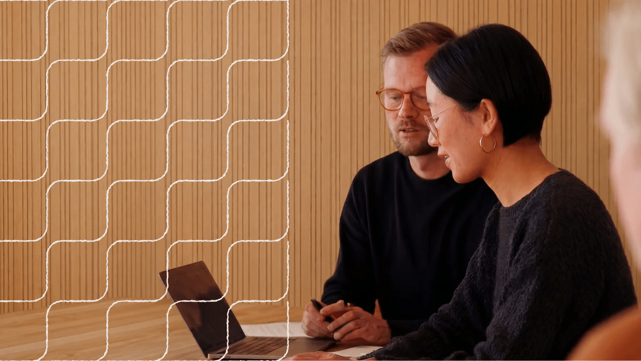 Two people seated at a table, looking at a laptop in a wood-paneled meeting room.