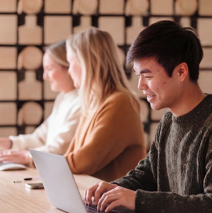 Professionals working side by side on laptops in an office.