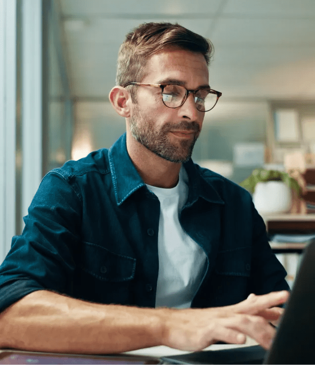 Office professional working on a laptop in a modern newsroom environment.