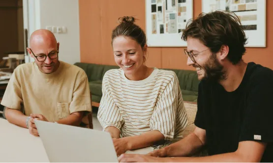 Three colleagues gathered around a laptop during a collaborative meeting.