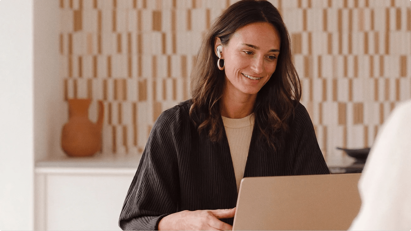 Person wearing wireless earbuds smiling while working on a laptop.