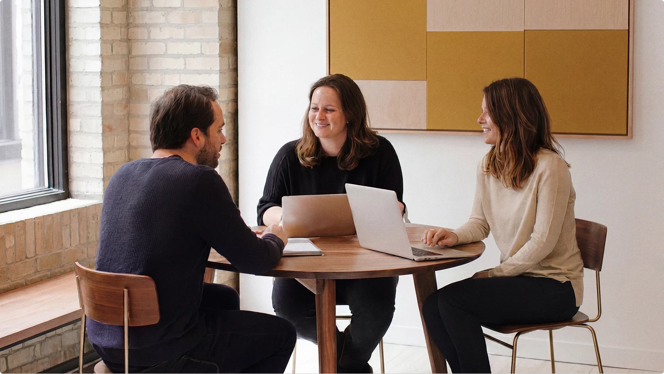 Three people seated around a table collaborating with laptops.