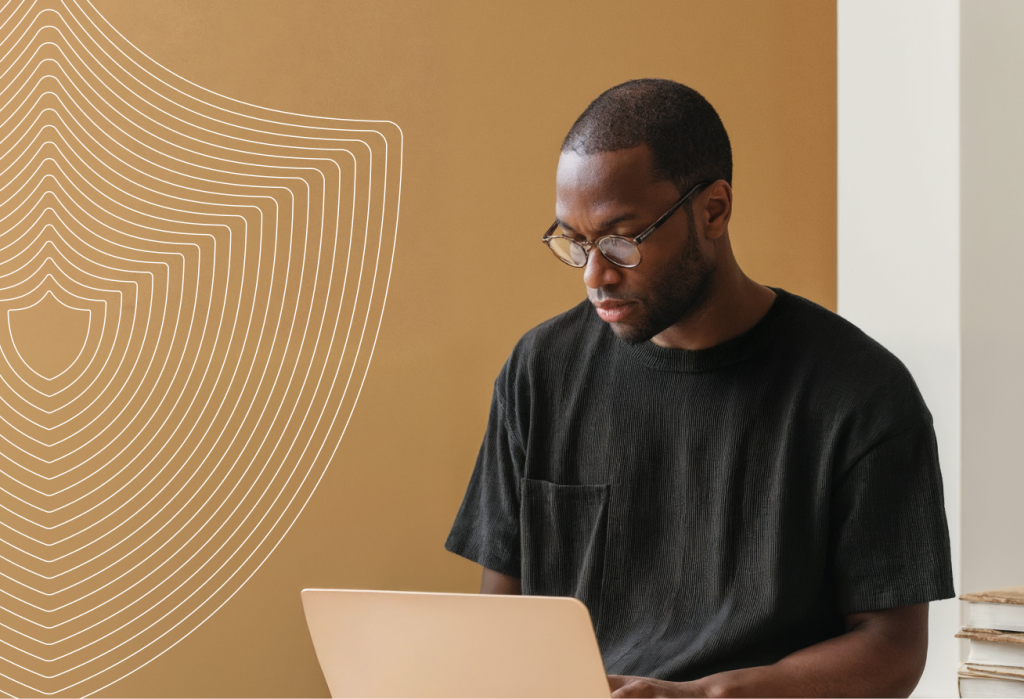 Professional using a laptop with a security shield illustration in the background.