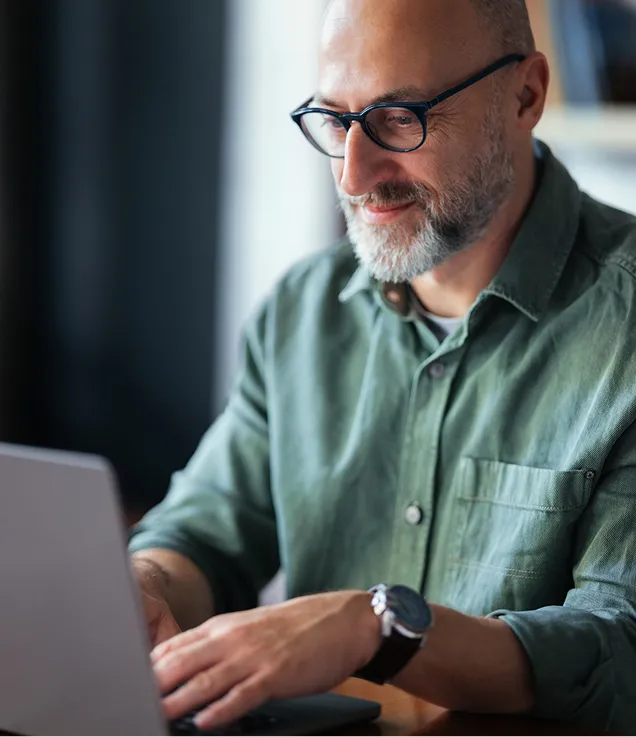 Person wearing glasses typing on a laptop while working at a desk.