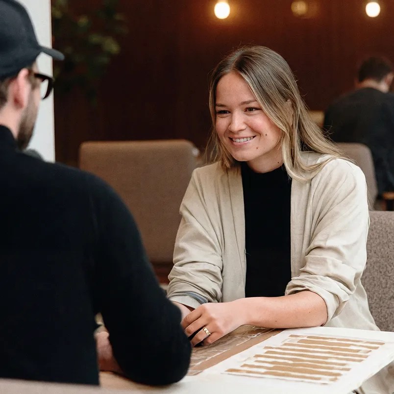 Two colleagues meeting across a table and reviewing materials together, representing the collaborative culture behind the enterprise content platform trusted by leading global organizations.