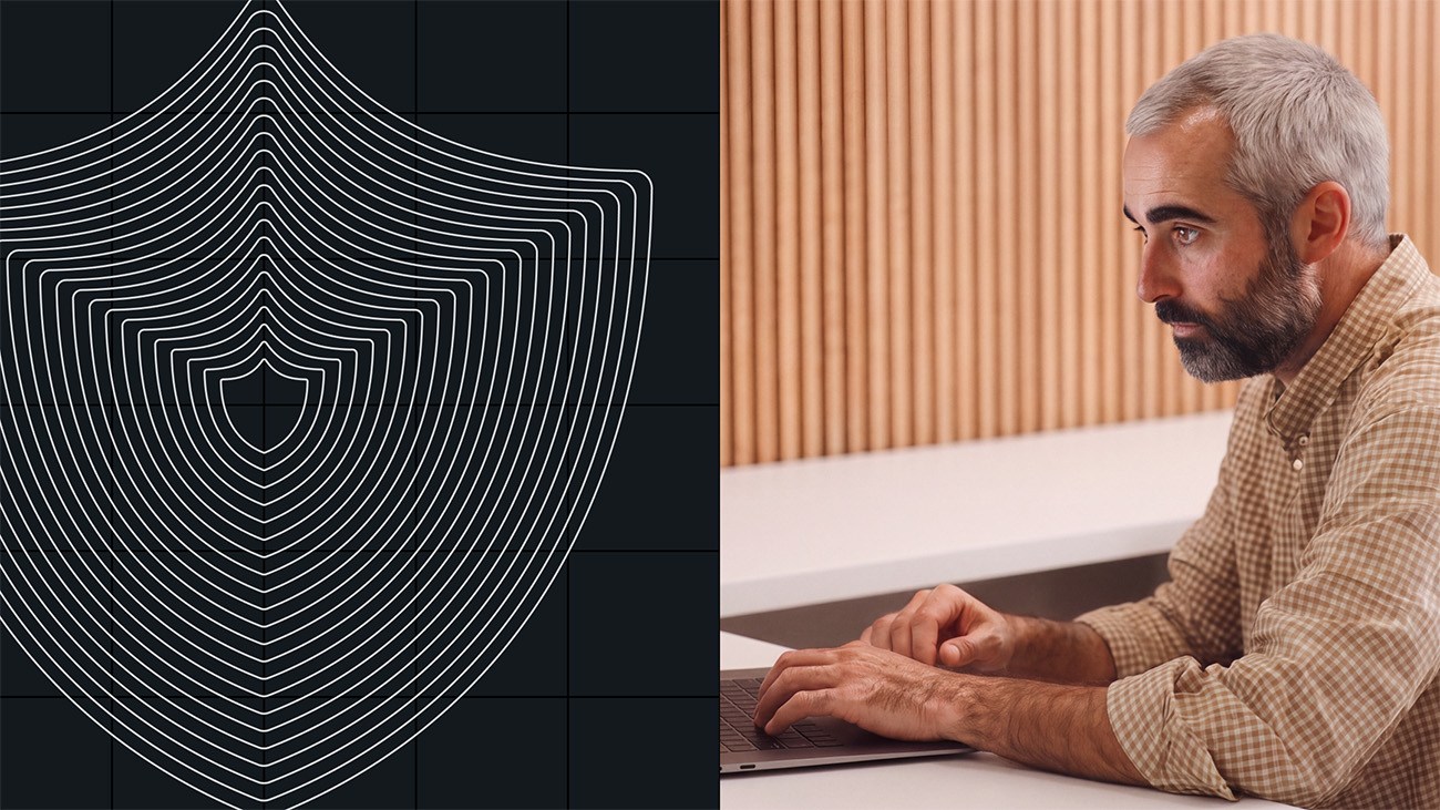 A man uses a laptop next to a graphic of layered shield outlines on a black background, symbolizing the importance of CISO buy-in for robust cybersecurity.