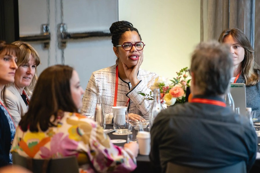 A group of people sits around a table in discussion at the Innovation Exchange event, with flowers and drinks in the center.