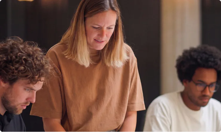 Three people sitting and working together at a table, focusing intently on something out of view—perhaps collaborating on a project with the help of an AI analytics assistant.