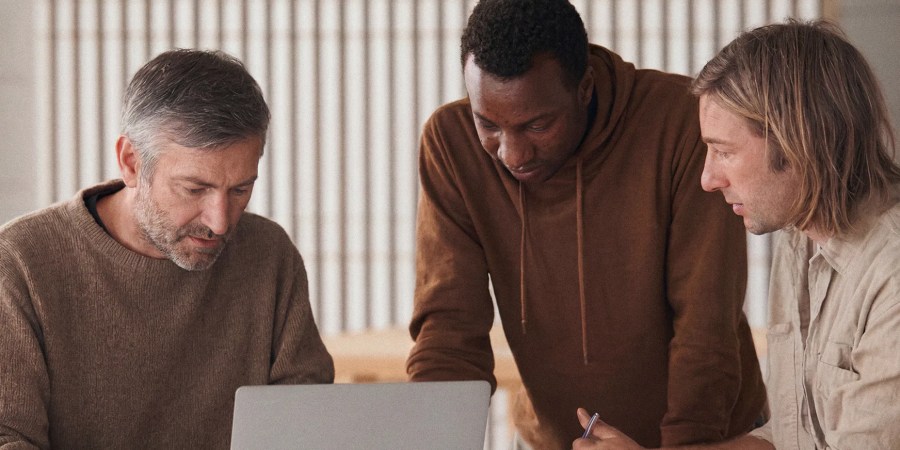 Three men collaborate while looking at a laptop in a bright, modern office setting, exploring insights powered by content analytics AI assistant tools.