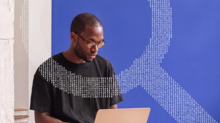 Man with glasses works on laptop; a search magnifier made of letters appears in the background against a blue wall, symbolizing the intricate connections of wordpress seo.