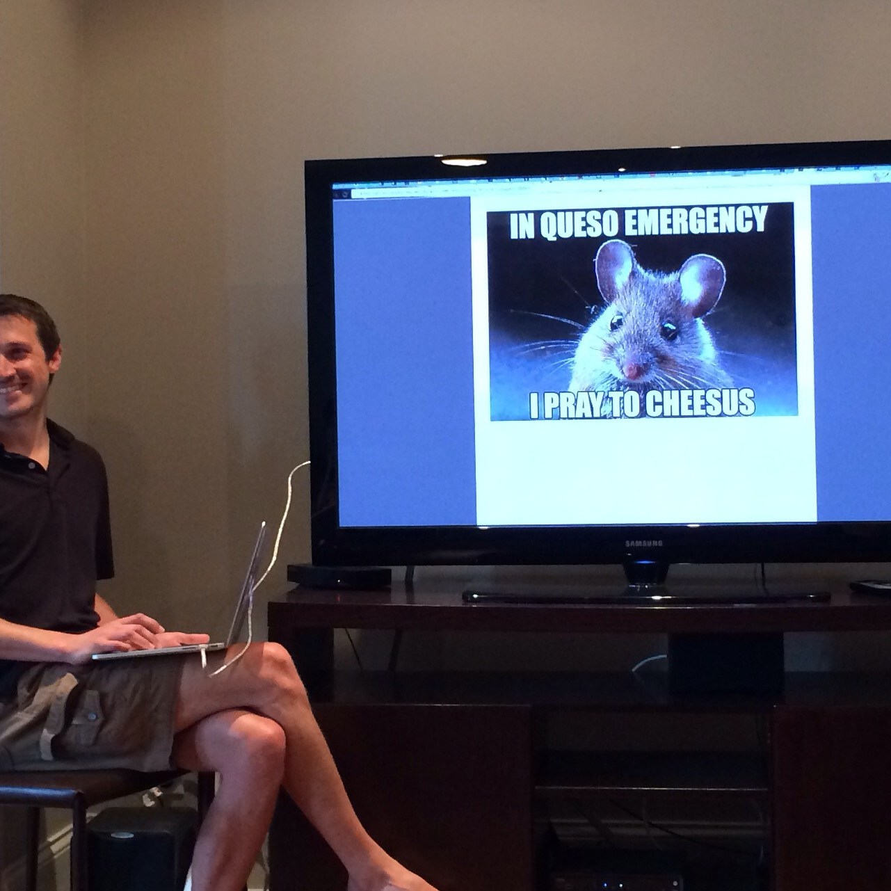 A presenter and slide at a team training session in Chicago. The slide has a picture of a meme that contains a picture of a mouse with the text "In queso emergency, I pray to cheesus."