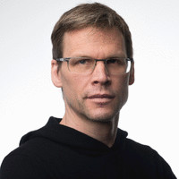 A headshot of Gordon Edall wearing glasses and a black hoodie