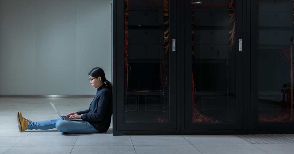 Person using a computer sitting next to a rack of servers